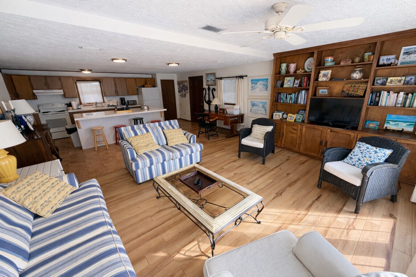 A spacious living room with a kitchen area, a dining table, and a bookshelf filled with books and decorations.