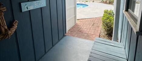 A covered porch with a bench, a sign reading "Doc Beach", and a view of a backyard with a pool and a fence.