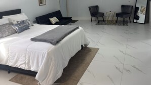 A modern bedroom with a large bed, a desk, and a chair. There is a door and an air conditioning unit on the wall. - Spacious, Beautiful Studio in Peaceful Miramar with Refreshing Ac (Miramar)