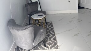 A room with a grey sofa, a small round table, a painting, a TV, and a door. - Spacious, Beautiful Studio in Peaceful Miramar with Refreshing Ac (Miramar)