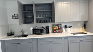 A modern kitchen with grey cabinets, a microwave, a coffee maker, and a snack rack. - Spacious, Beautiful Studio in Peaceful Miramar with Refreshing Ac (Miramar)