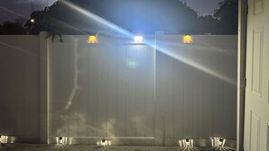 A white wooden fence with a door, illuminated by overhead lights. - Spacious, Beautiful Studio in Peaceful Miramar with Refreshing Ac (Miramar)