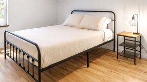 A single bed with a metal frame, a wooden nightstand with a lamp, and a window providing natural light. - Charming 3-bedroom cabin near Mt. Rainier with AC-Hot Tub-WiFi (Ashford)