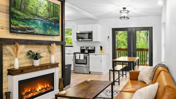 A modern living room with a fireplace, a sofa, a dining table, and a kitchen in the background. - Charming 3-bedroom cabin near Mt. Rainier with AC-Hot Tub-WiFi (Ashford)