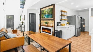 A modern kitchen with a central island, a dining area with a wooden table and benches, and a living room with a leather sofa and a fireplace. - Charming 3-bedroom cabin near Mt. Rainier with AC-Hot Tub-WiFi (Ashford)