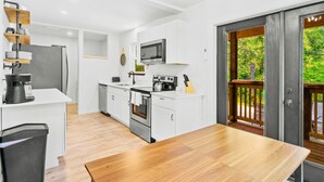 A modern kitchen with white cabinets, stainless steel appliances, and a wooden dining table. - Charming 3-bedroom cabin near Mt. Rainier with AC-Hot Tub-WiFi (Ashford)