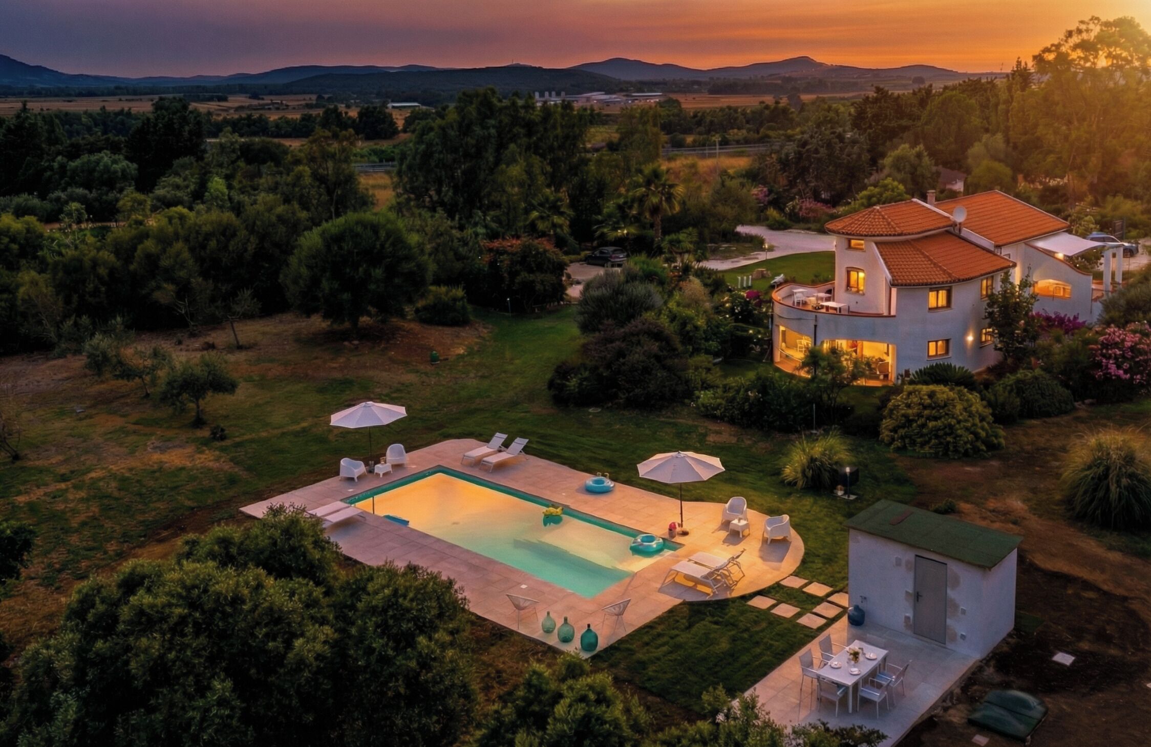 A modern house with a swimming pool, surrounded by lush greenery and hills in the background.