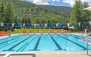 Una piscina con corsie, lettini da relax rossi e bianchi e montagne sullo sfondo.