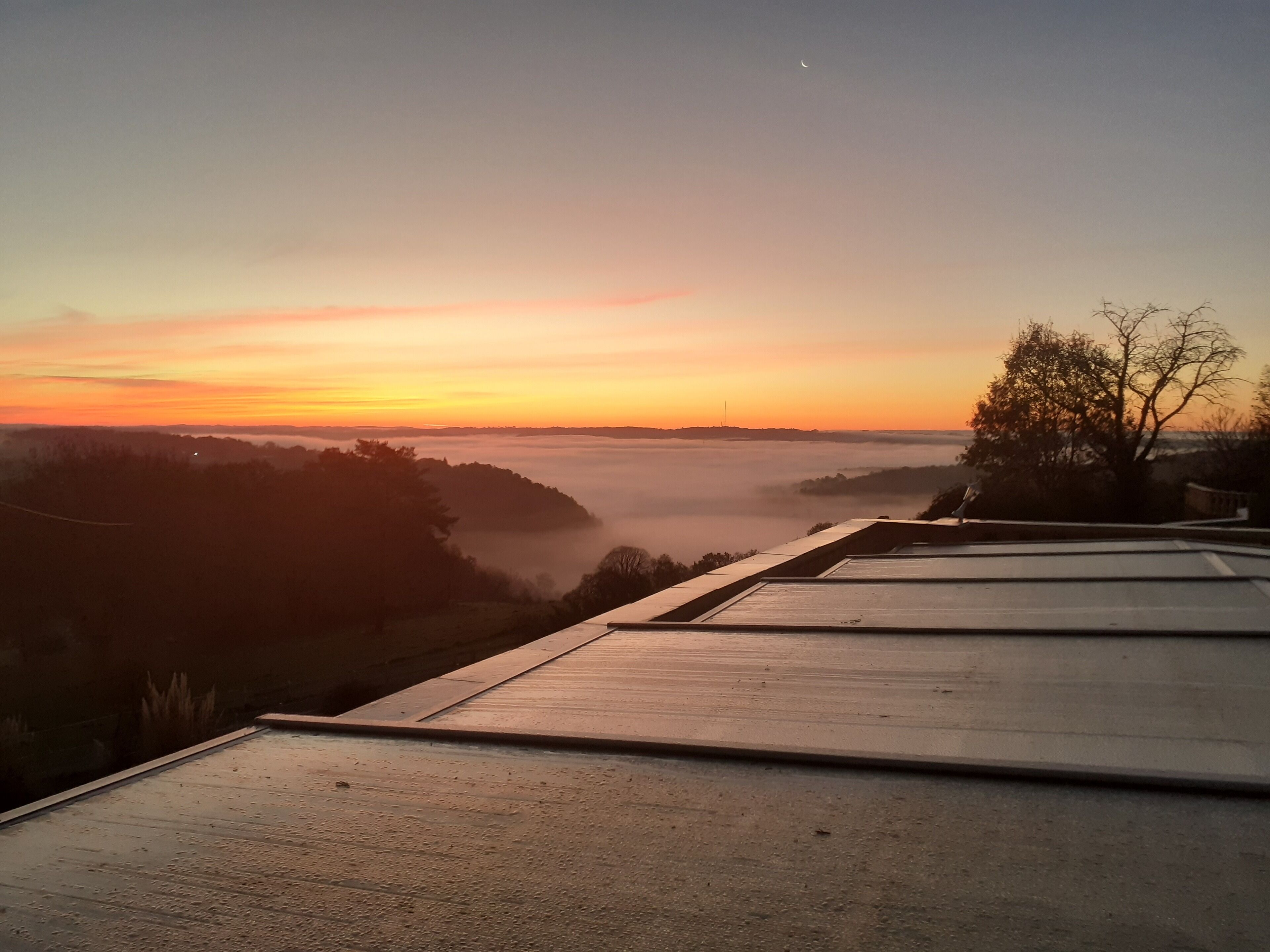 Sonnenaufgangsblick von einer Dachterrasse mit Betonboden und einem Baum im Vordergrund.