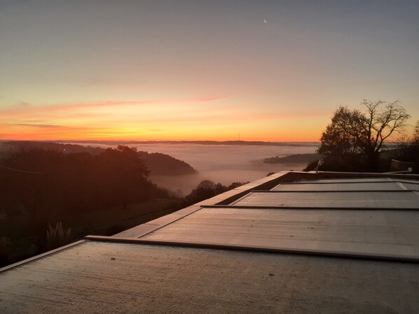 A sunrise view from a rooftop terrace with a concrete floor and a tree in the foreground. - DOMAINE DE SWEENDY GITE LE PANORAMIQUE (Le Bugue)