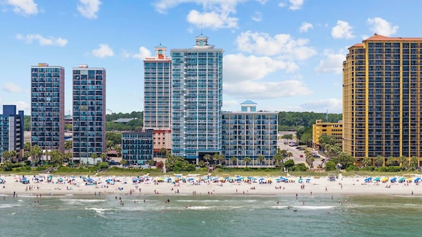 A beachfront hotel with multiple high-rise buildings, a sandy beach, and a clear sky. - NEW fireplace and Christmas Decor starts Nov 1! (Myrtle Beach)
