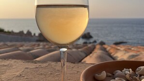 Un verre de vin blanc sur une terrasse offrant une vue sur la mer et les formations rocheuses.