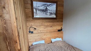 A bedroom with a wooden headboard, a mounted picture of a snowy landscape, a bed with a patterned blanket, and bedside lamps. - Le Menhir, Chalets de Lady (Megève)