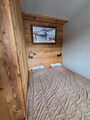 Un dormitorio con cabecera de madera, un cuadro colgado de un paisaje nevado, una cama con manta estampada y lámparas de noche.