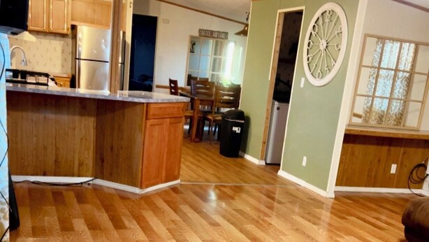 A spacious living area with hardwood flooring, a kitchen with wooden cabinets, a dining table, and a clock on the wall.