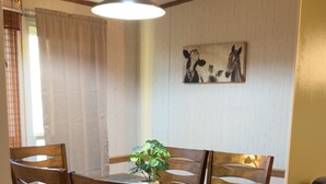 A dining area with a wooden table and chairs, a hanging light fixture, and a wall-mounted painting.