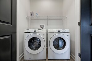 A laundry room with two white Samsung front-loading washing machines and a shelf above them.