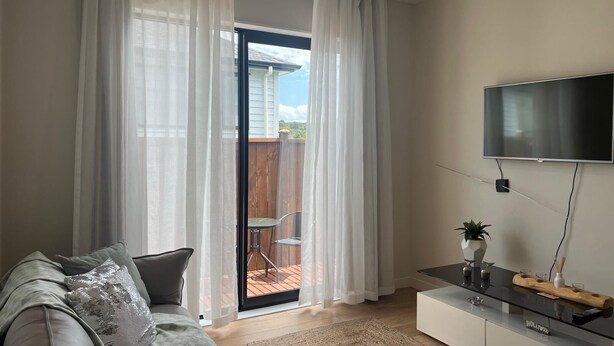 Una sala moderna con un sofá, un televisor montado en la pared y un ventanal corredero que da a un patio exterior.