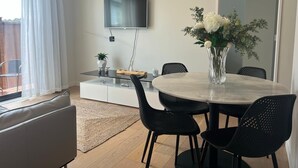 Un comedor moderno con una mesa redonda, sillas negras, un florero con flores, un televisor de pantalla plana montado en la pared y una mesa de vidrio.