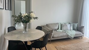 Una sala de estar moderna con una mesa de comedor redonda, sillas negras, un sofá gris con una manta y un ventanal con cortinas.