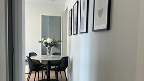 Un área de comedor moderna con una mesa blanca y sillas negras, un florero con flores blancas y cuadros en la pared.