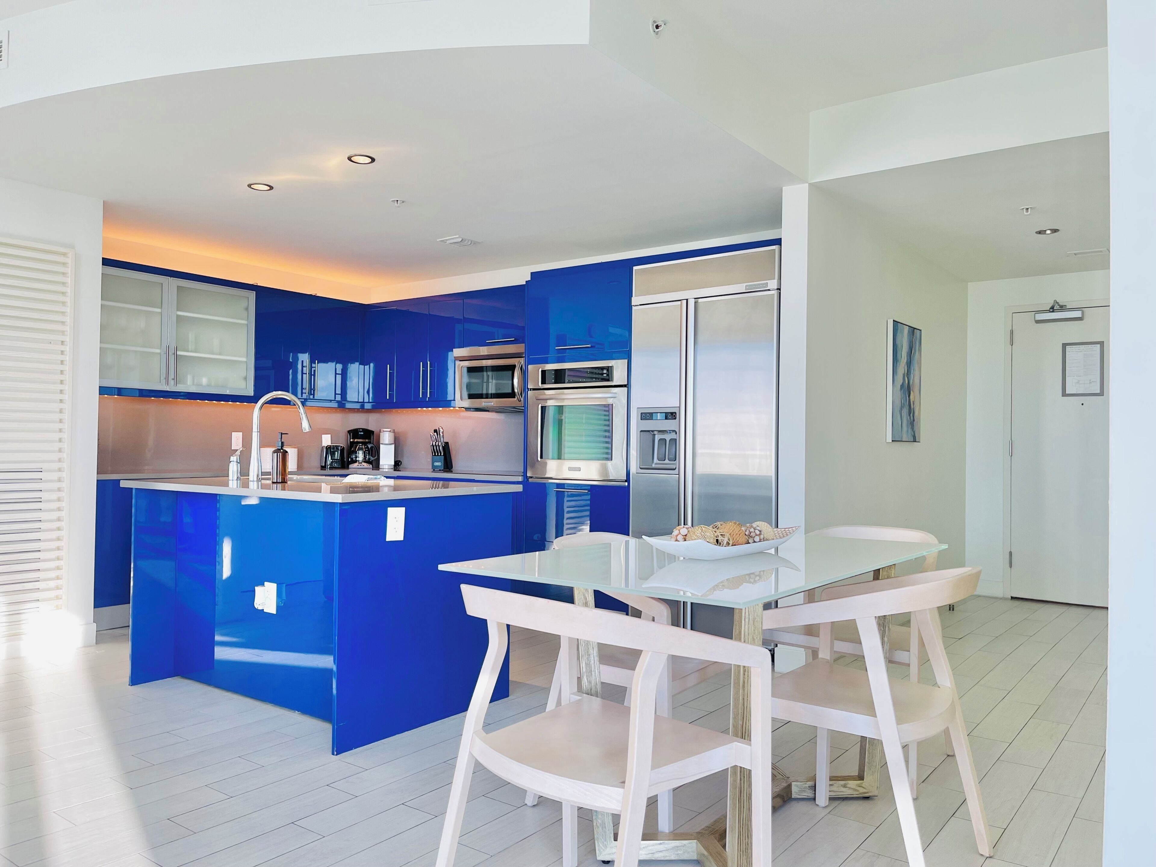 A modern kitchen with blue cabinets, a central island, and a dining area with white chairs.