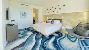 Ein modernes Hotelzimmer mit einem großen Bett, einem Schreibtisch mit Computer, einem Sessel und einer Wandverzierung.