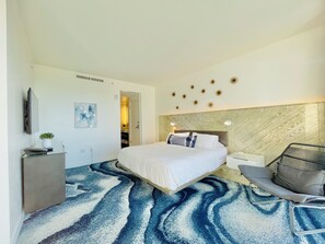 Een moderne hotelkamer met een groot bed, een bureau met computer, een stoel en een decoratieve wand.