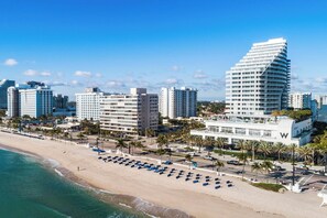 Een strandhotel met meerdere hoge gebouwen, een zandstrand en een helderblauwe lucht.