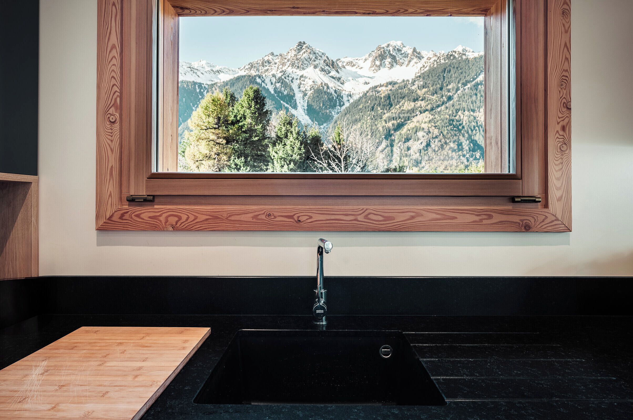 A kitchen with a wooden countertop, a black sink, and a window with a view of mountains.