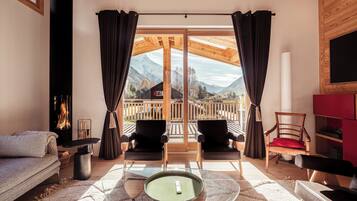 A cozy living room with a sofa, two chairs, a glass coffee table, and a view of mountains through large windows.