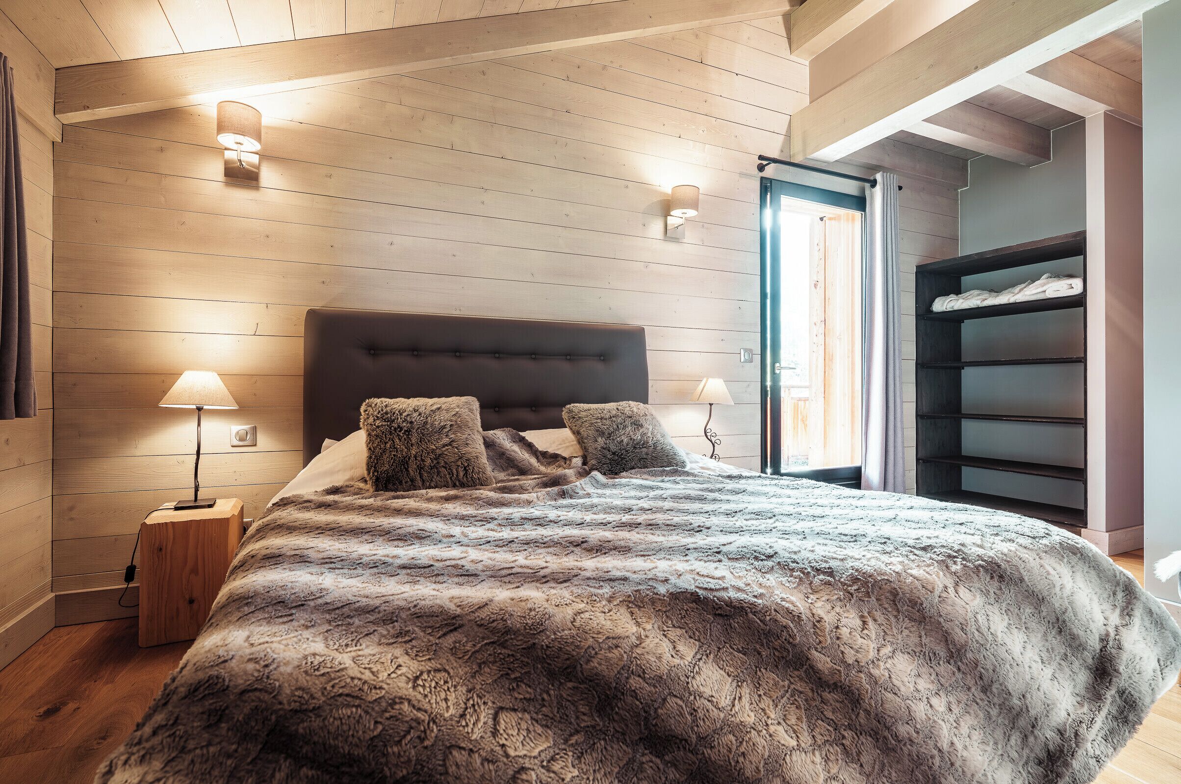 A bedroom with a wooden ceiling, a large bed with a fluffy blanket, two bedside lamps, and a built-in wardrobe.