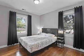 A bedroom with a large bed, two bedside tables with lamps, and windows with curtains. - Spacious Des Plaines Home - Near Airport, Casino & Arena (Des Plaines)