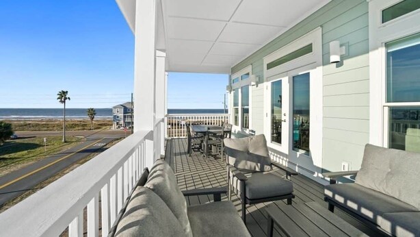 Uma varanda com vista para a praia, um espaço de estar com mesa e um corrimão.