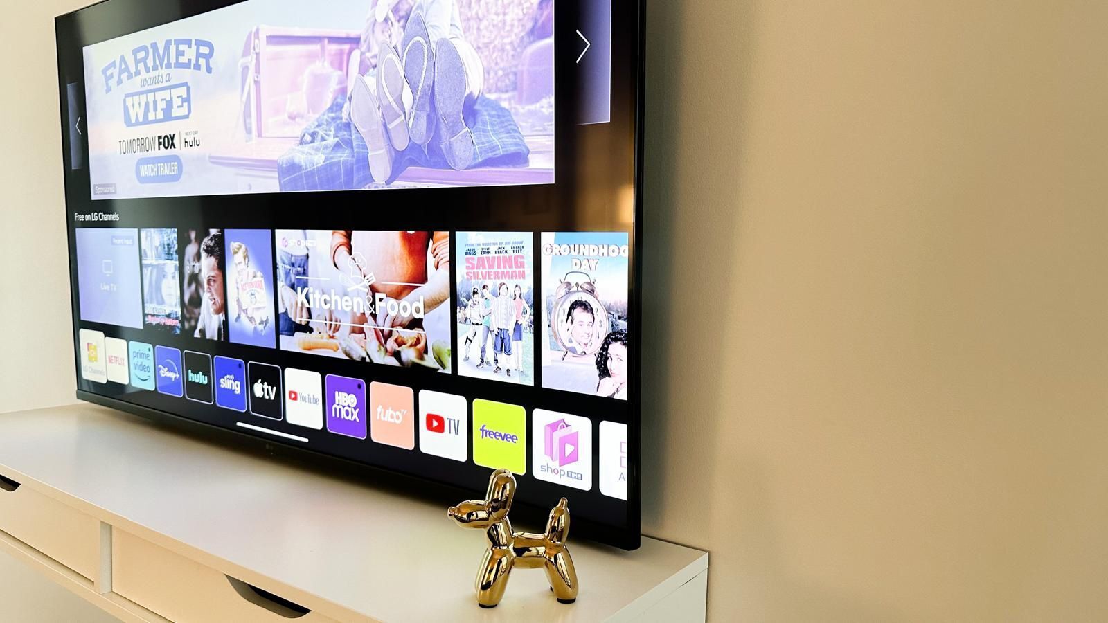 Un televisor de pantalla plana sobre un soporte blanco mostrando varios servicios de streaming y un avance de la película "Farmer Wants a Wife" en Hulu.