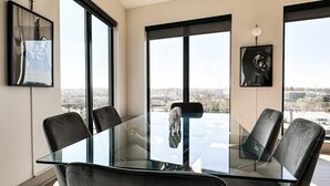 Een moderne vergaderruimte met een glazen tafel en zwarte lederen stoelen, grote ramen met uitzicht op de stad, en kunstwerken aan de wanden.