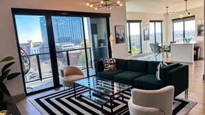 Een moderne woonkamer met een glazen salontafel, een donkergroene bank en een beige fauteuil.