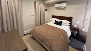 Ein Schlafzimmer mit Bett, Vorhängen, Nachttisch, Lampe und Klimaanlage.