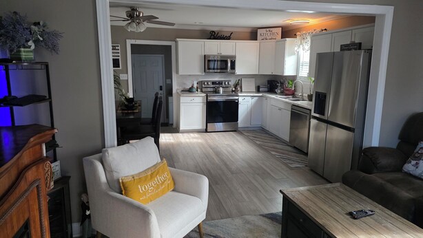 A modern kitchen with white cabinets, stainless steel appliances, and a ceiling fan.