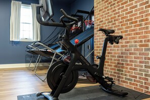 Un vélo d’appartement dans une pièce dont un mur est en briques et qui possède une fenêtre avec des rideaux.
