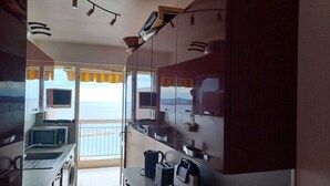 A compact kitchen with a view of the sea, a washing machine, a microwave, and a coffee maker. - Sea view apartment (Saint-Raphaël)