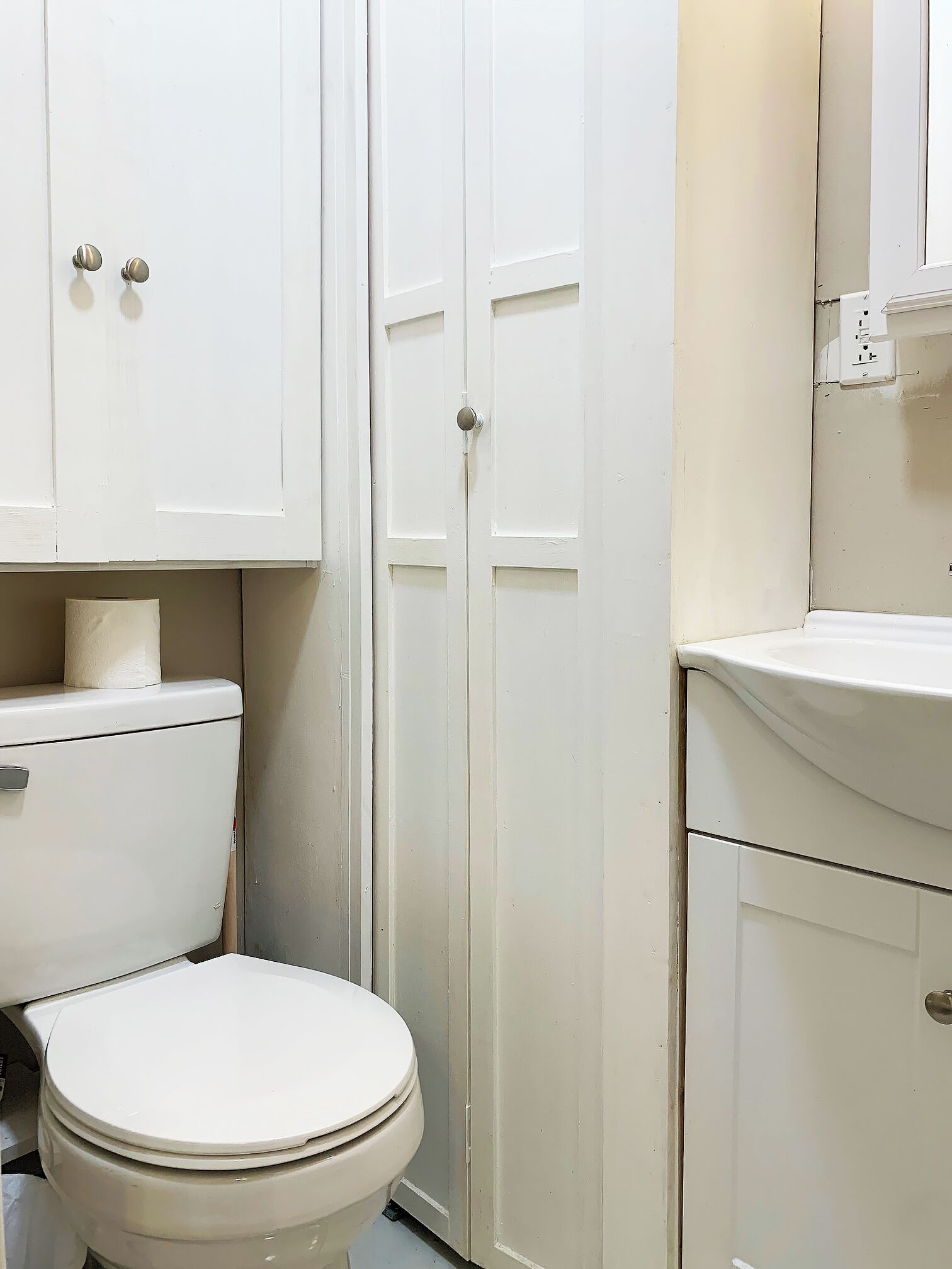 Un baño pequeño y blanco con inodoro, lavamanos y armario.
