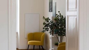 A hallway with a wooden floor, a yellow armchair, a whiteboard, and a potted plant. - Bright apartment in the city center (Graz)