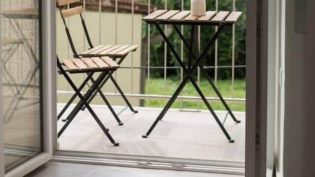 A balcony with a wooden chair, a small table, and a vase of flowers. - Bright apartment in the city center (Graz)