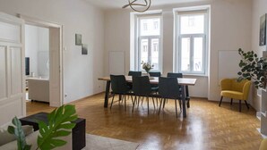 A spacious room with a wooden floor, a dining table with chairs, large windows, and a yellow armchair. - Bright apartment in the city center (Graz)
