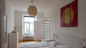 A bedroom with a bed, a white wardrobe, a window, a hanging light fixture, and two red paintings on the wall. - Bright apartment in the city center (Graz)