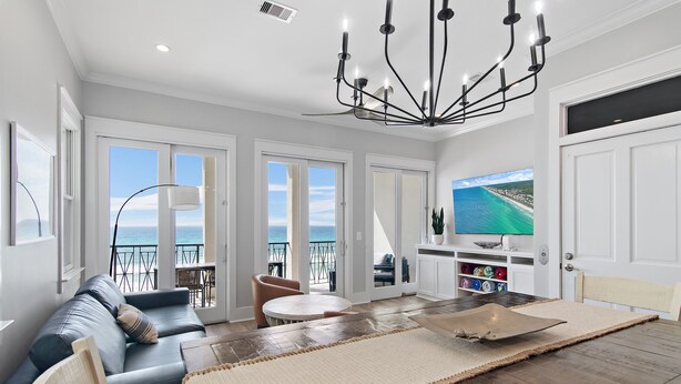 A modern living room with a sofa, a dining table, and a TV displaying a scenic view. - Frangista Sunset | Private Beach | Pools | Updated | Beach Gear | 3 Patios (Miramar Beach)