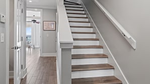 A staircase with wooden steps and white railings, leading to a room with a view of the outdoors. - Frangista Sunset | Private Beach | Pools | Updated | Beach Gear | 3 Patios (Miramar Beach)