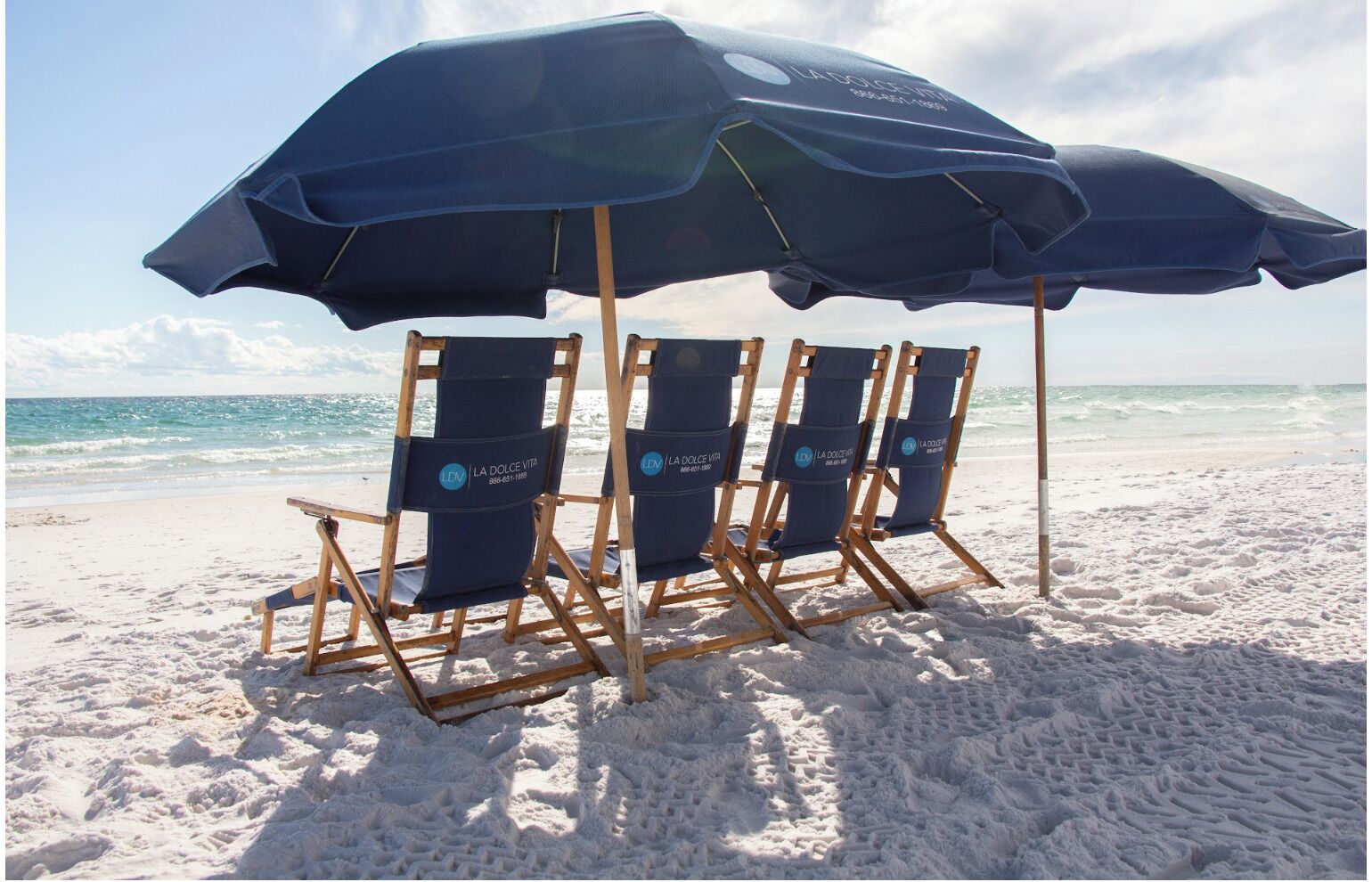 Ein Strand mit vier Holzliegen unter einem großen, blauen Sonnenschirm.