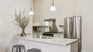 Una cocina moderna con un refrigerador de acero inoxidable, una estufa a gas, una encimera de mármol y dos taburetes de bar.